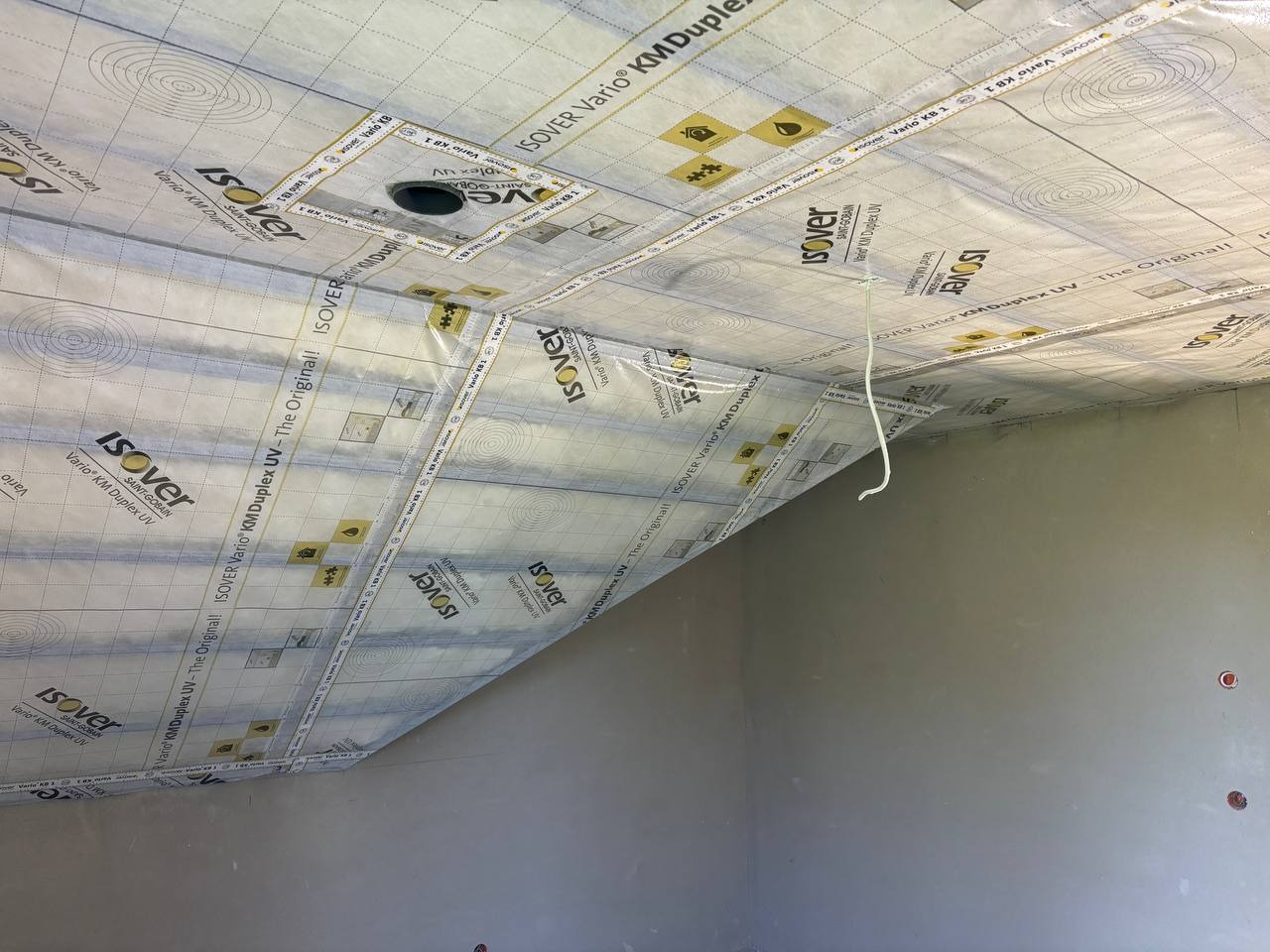 Poddasze w trakcie ocieplania: widoczna folia paroizolacyjna Isover Vario KM Duplex UV, zabezpieczająca przed wilgocią. Fragment ściany z otworem na gniazdko.