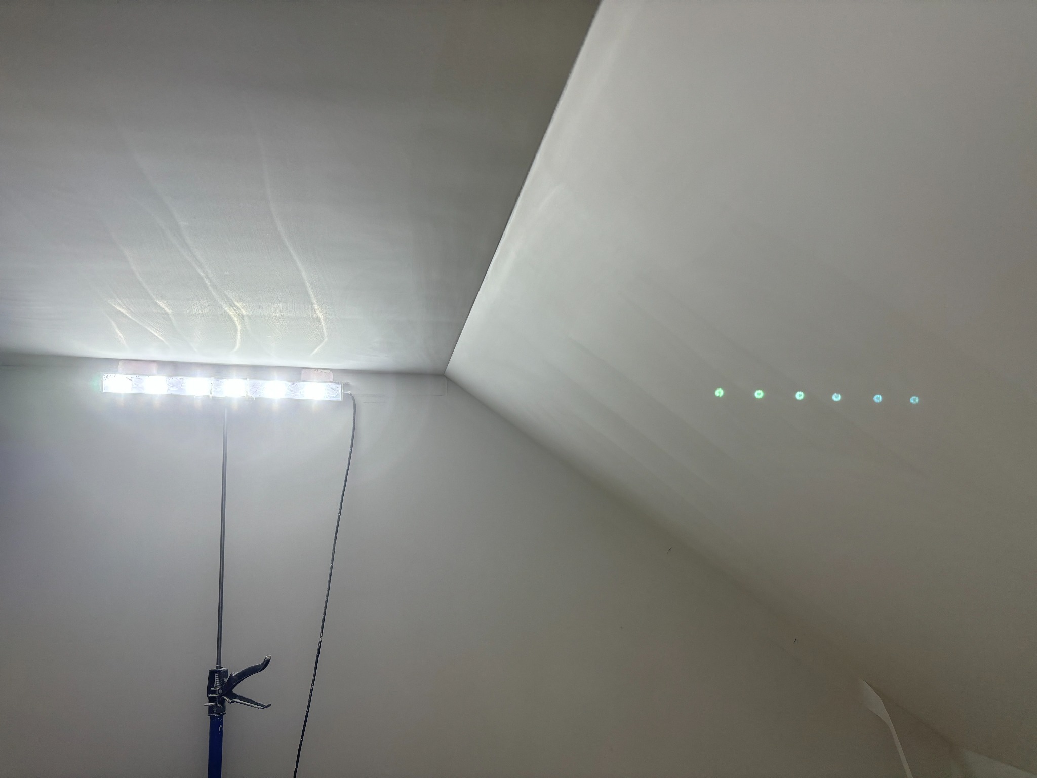 Wykończone poddasze ze skośnym sufitem oświetlone listwą LED, ukazując gładką, pomalowaną powierzchnię. Widoczne refleksy świetlne na ścianie.