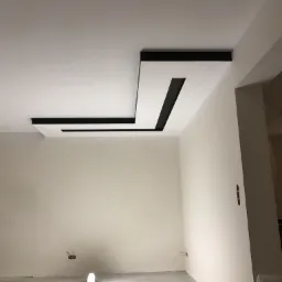 Nowoczesny sufit podwieszany z czarnymi wstawkami, oświetlenie robocze na podłodze, surowy stan wykończenia wnętrza.