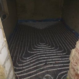 Daw-Instal - Rozłożone rury ogrzewania podłogowego na siatce w surowym pomieszczeniu z fragmentami muru i tynku.