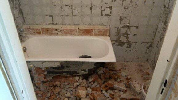 Demontaż starej wanny w łazience, widoczne gruz i odłupane płytki, przygotowanie do remontu.