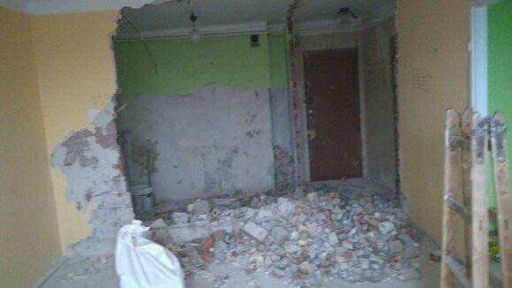 Demontaż ściany działowej z odsłoniętą cegłą i gruzem na podłodze, widoczna drabina oparta o ścianę w trakcie prac remontowych.