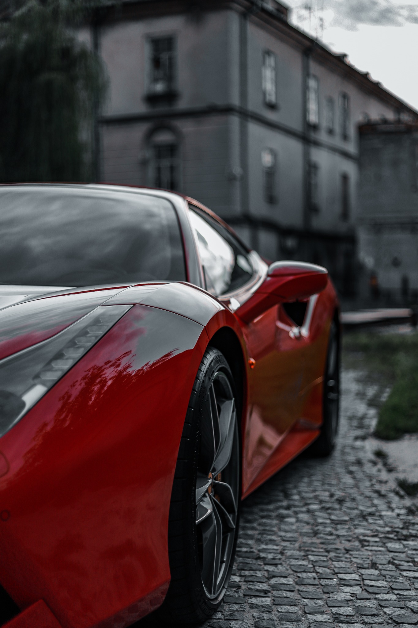 Czerwony sportowy samochód na brukowanej drodze z rozmytym budynkiem w tle.