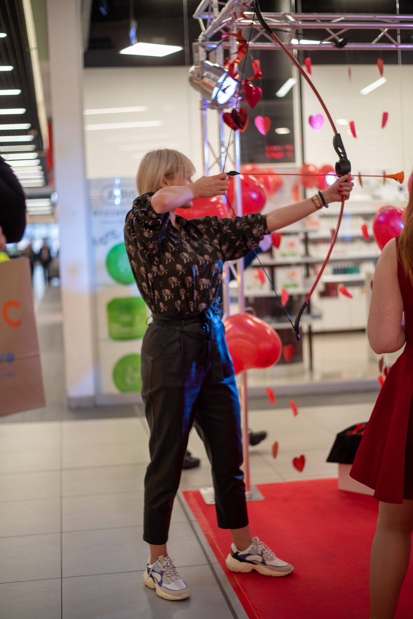 Kobieta celuje z łuku w serca podczas walentynkowej zabawy, czerwony dywan, białe tło, oświetlenie sceniczne.