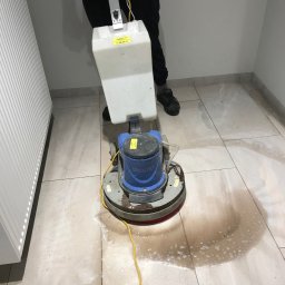 Pozamiatane - Czyszczenie podłogi z płytek za pomocą profesjonalnej maszyny czyszczącej. Widoczne zabrudzenia i woda na powierzchni. Praca w trakcie wykonywania.