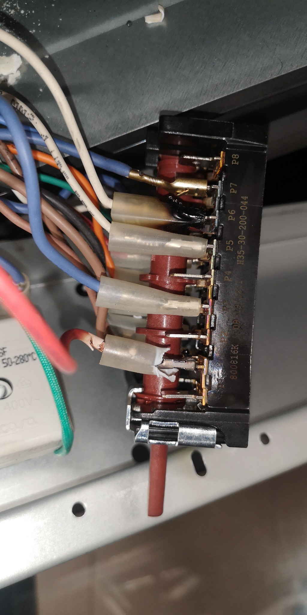 Wnętrze zmywarki z widocznym uszkodzonym modułem sterującym, stopione elementy plastikowe i przypalone kable wskazują na awarię elektryczną.