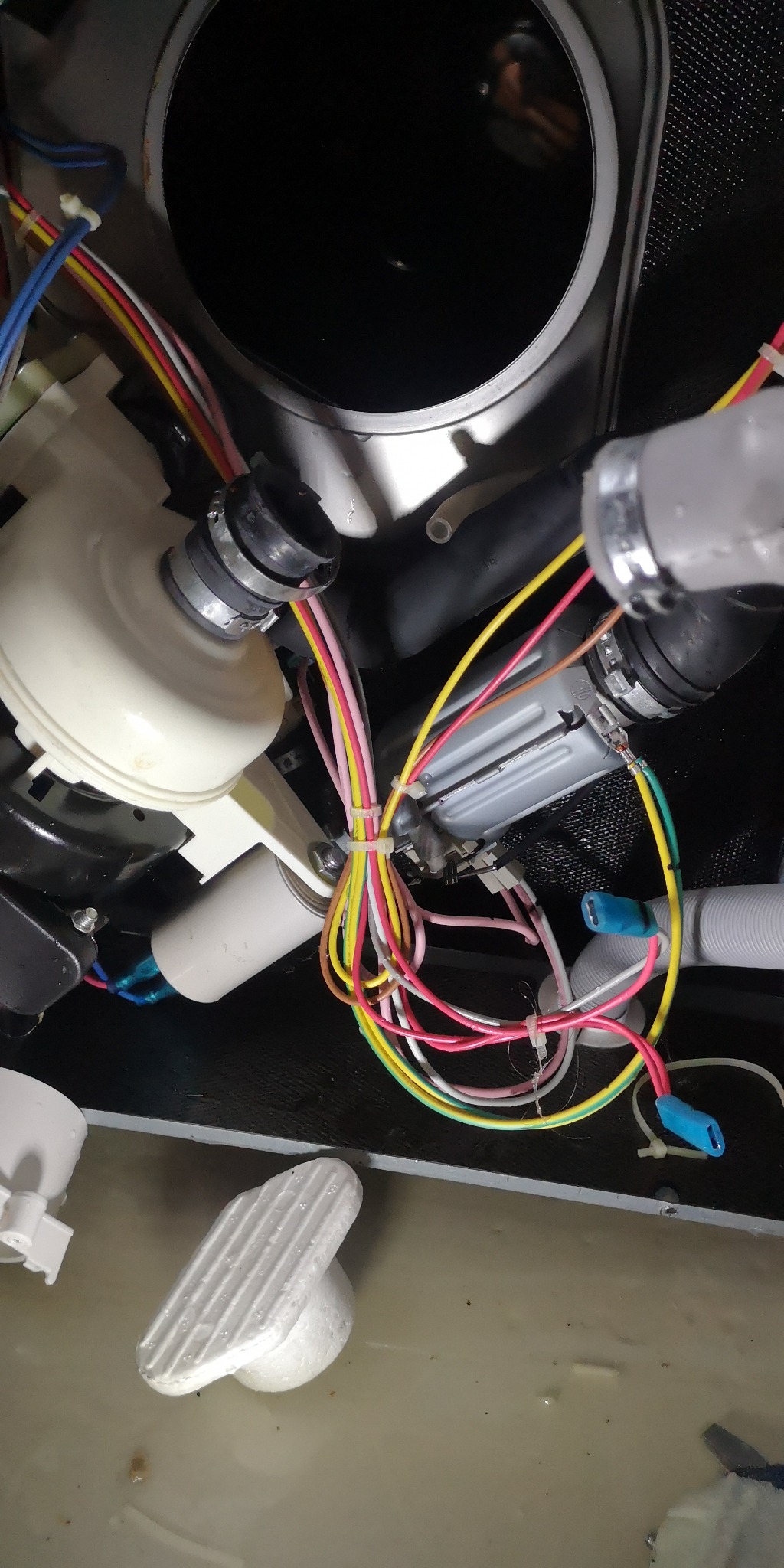 Wnętrze zmywarki z widocznymi elementami pompy, przewodami elektrycznymi spiętymi opaskami zaciskowymi i stojącą wodą na dnie.