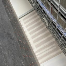 Firma Usługowa Simon - Wnętrze w trakcie prac: szpachlowane ściany z widocznymi pasami, metalowa konstrukcja sufitu i płytki na ścianie z krzyżykami dystansowymi. Ujęcie z dołu.