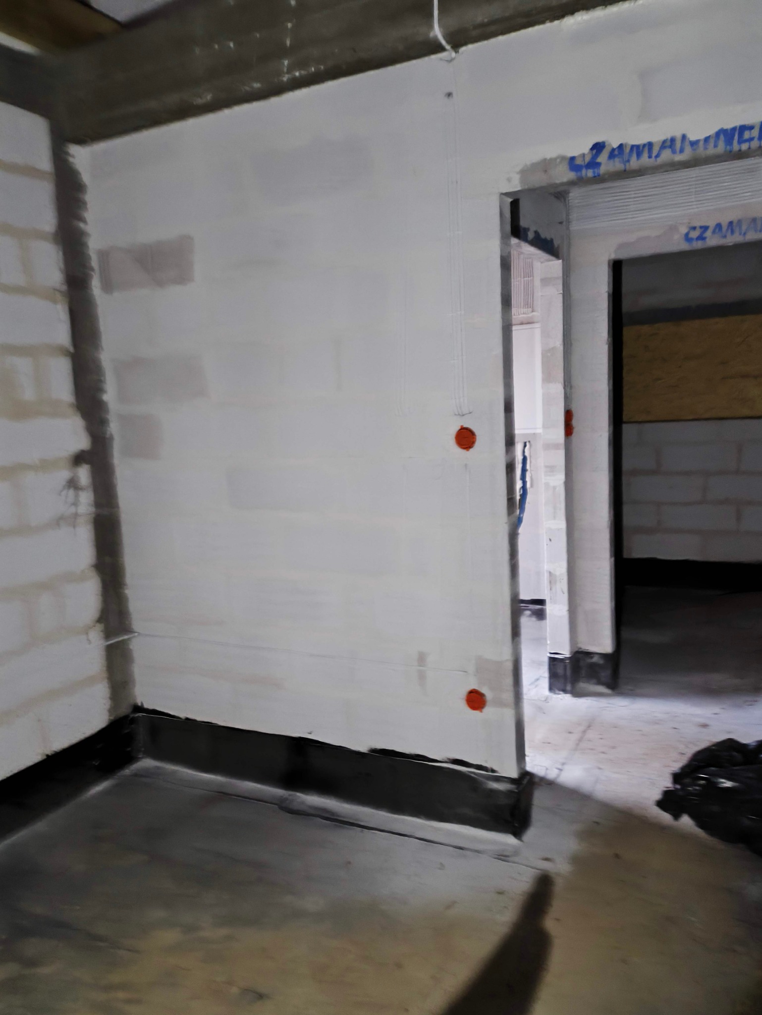 Surowy stan wnętrza z widocznymi puszkami instalacyjnymi na ścianie z betonu komórkowego, przygotowanego do dalszych prac wykończeniowych.