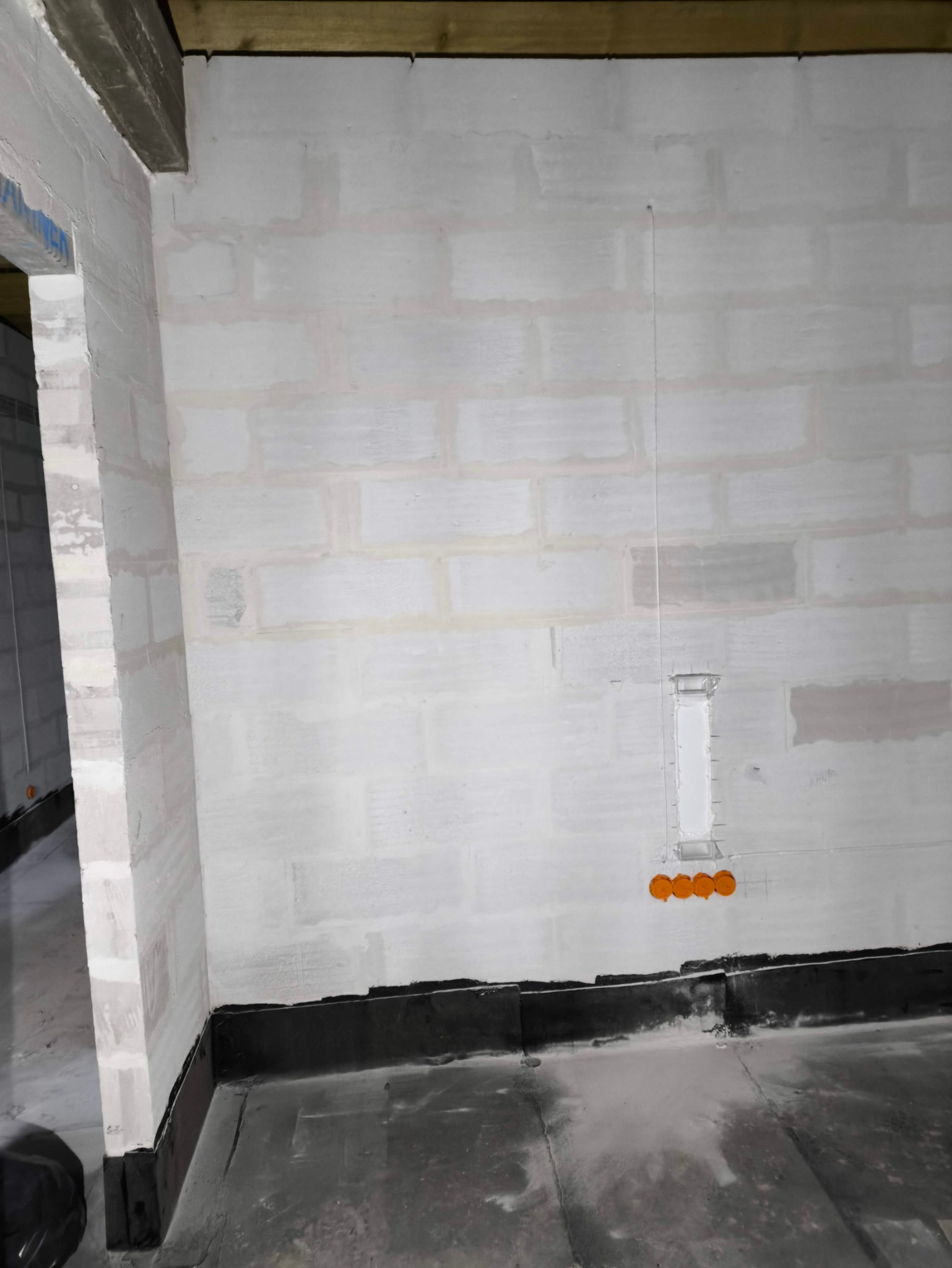 Surowa ściana z betonu komórkowego w trakcie prac wykończeniowych, widoczne puszki instalacyjne i pionowa bruzda pod przewody.