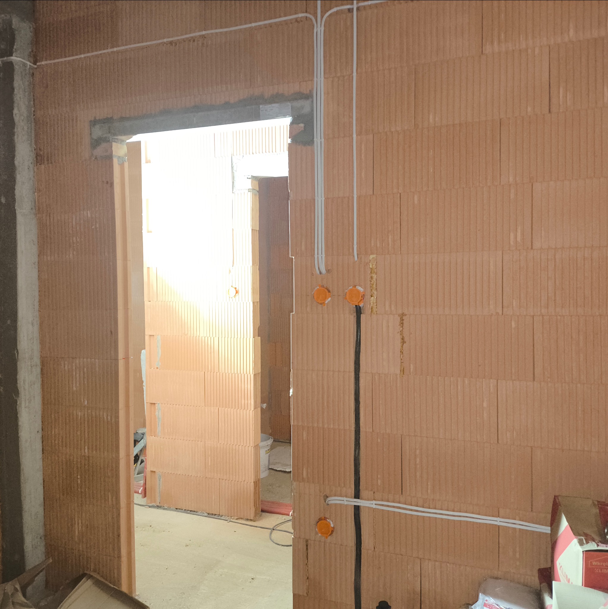 Ściana z pustaków ceramicznych z widocznymi przewodami elektrycznymi w peszlach i puszkami instalacyjnymi, fragment surowego wnętrza w trakcie prac wykończeniowych.