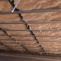 Poddasze z widoczną warstwą izolacji z wełny mineralnej umieszczoną między metalowymi profilami konstrukcyjnymi, zabezpieczoną folią. Widoczne niedociągnięcia w ułożeniu izolacji.