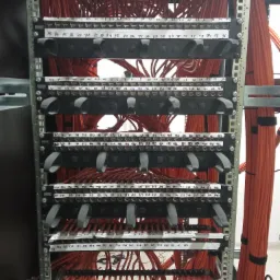 Panel krosowniczy z uporządkowanymi kablami sieciowymi w kolorze pomarańczowym, oznaczony numerami na białych etykietach, zainstalowany w szafie serwerowej.