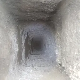 Wnętrze komina z widocznymi osadami sadzy na ścianach, sfotografowane z dołu do góry.