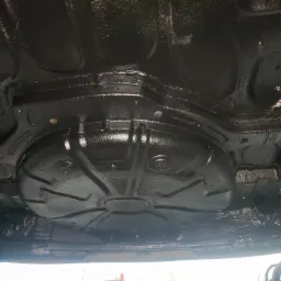 Spód samochodu po nałożeniu grubej warstwy czarnej powłoki antykorozyjnej, widoczne elementy konstrukcyjne i wzmocnienia