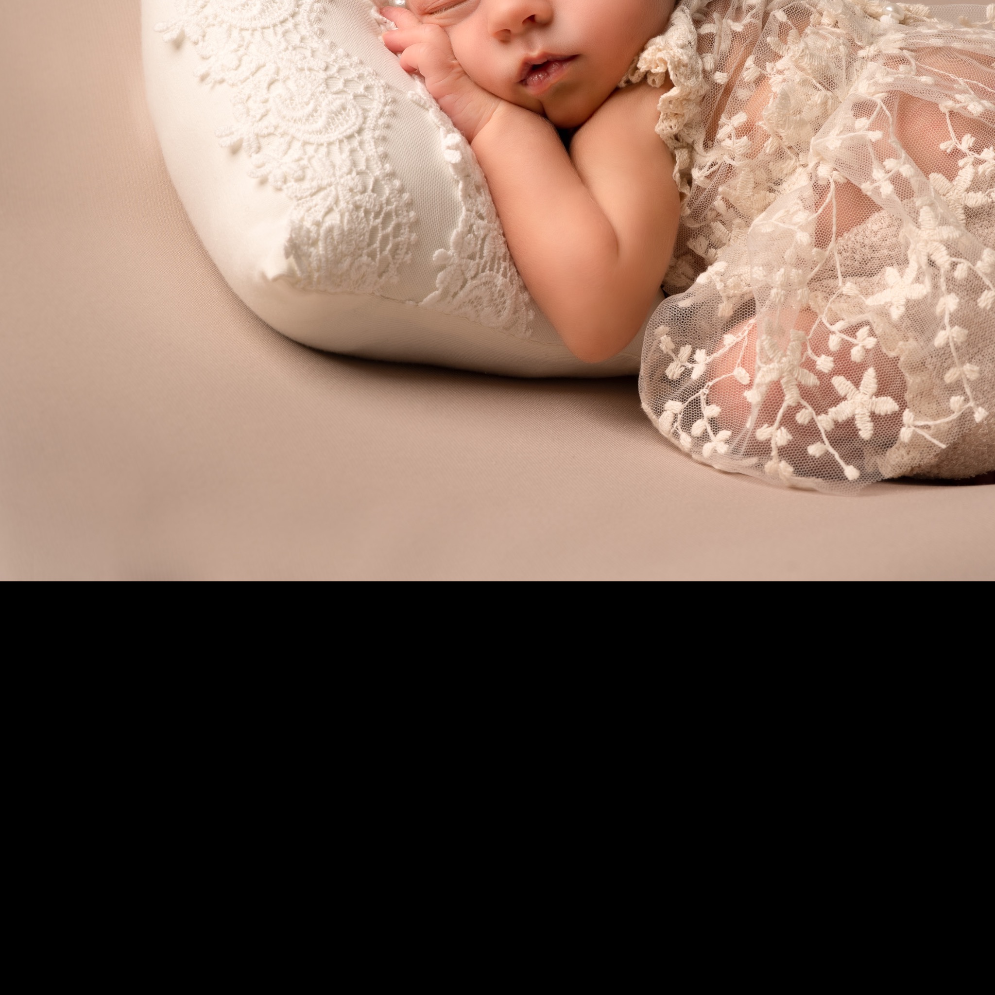 Śpiące niemowlę ułożone na koronkowej poduszce w dopasowanym, ażurowym okryciu.