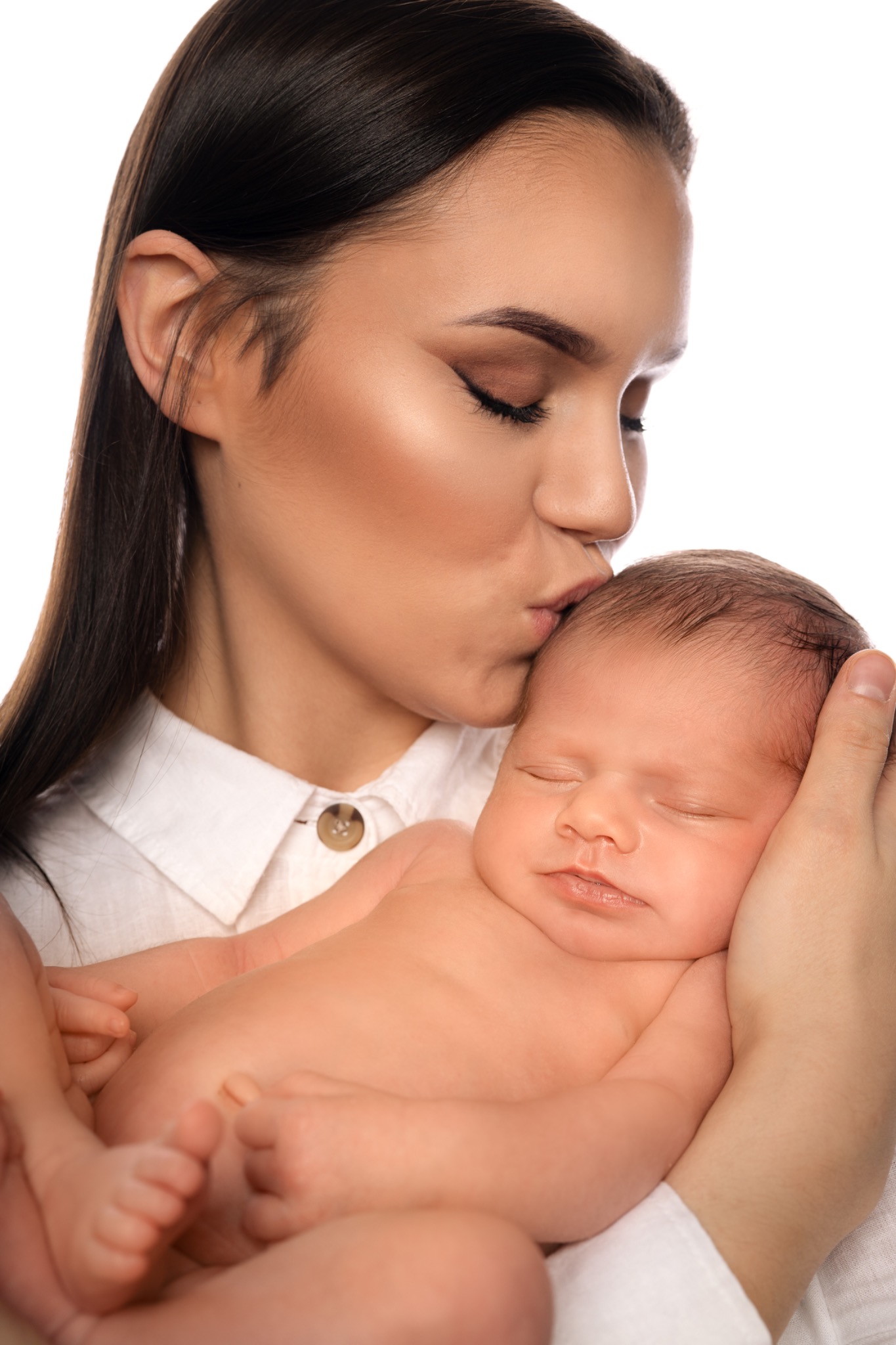 Delikatne ujęcie śpiącego noworodka w ramionach matki, która całuje go w czoło, wykonane w Bełchatowie, na białym tle.
