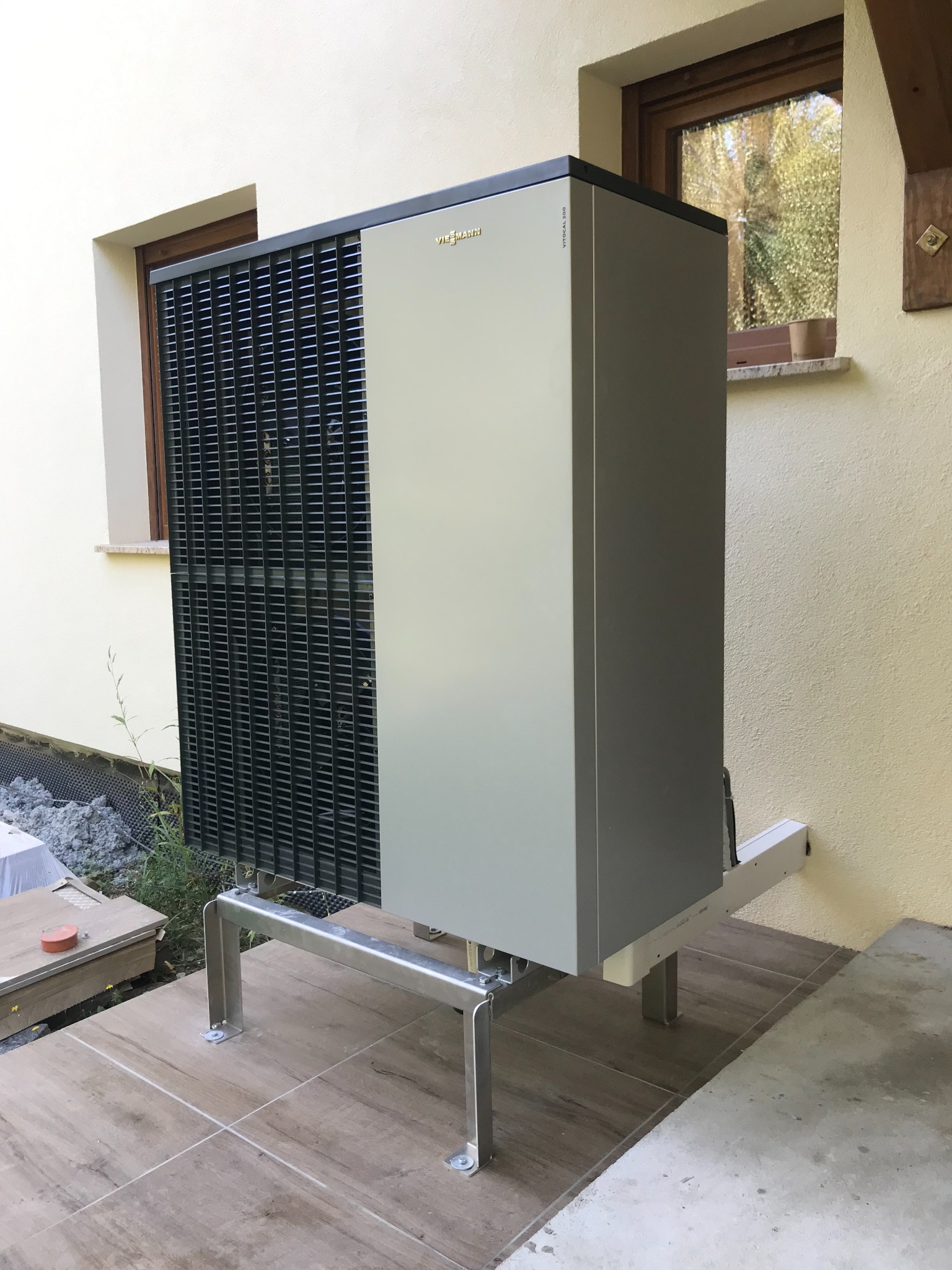 Zewnętrzna pompa ciepła marki Viessmann zamontowana na metalowej konstrukcji przy jasnej ścianie budynku z widocznym oknem.