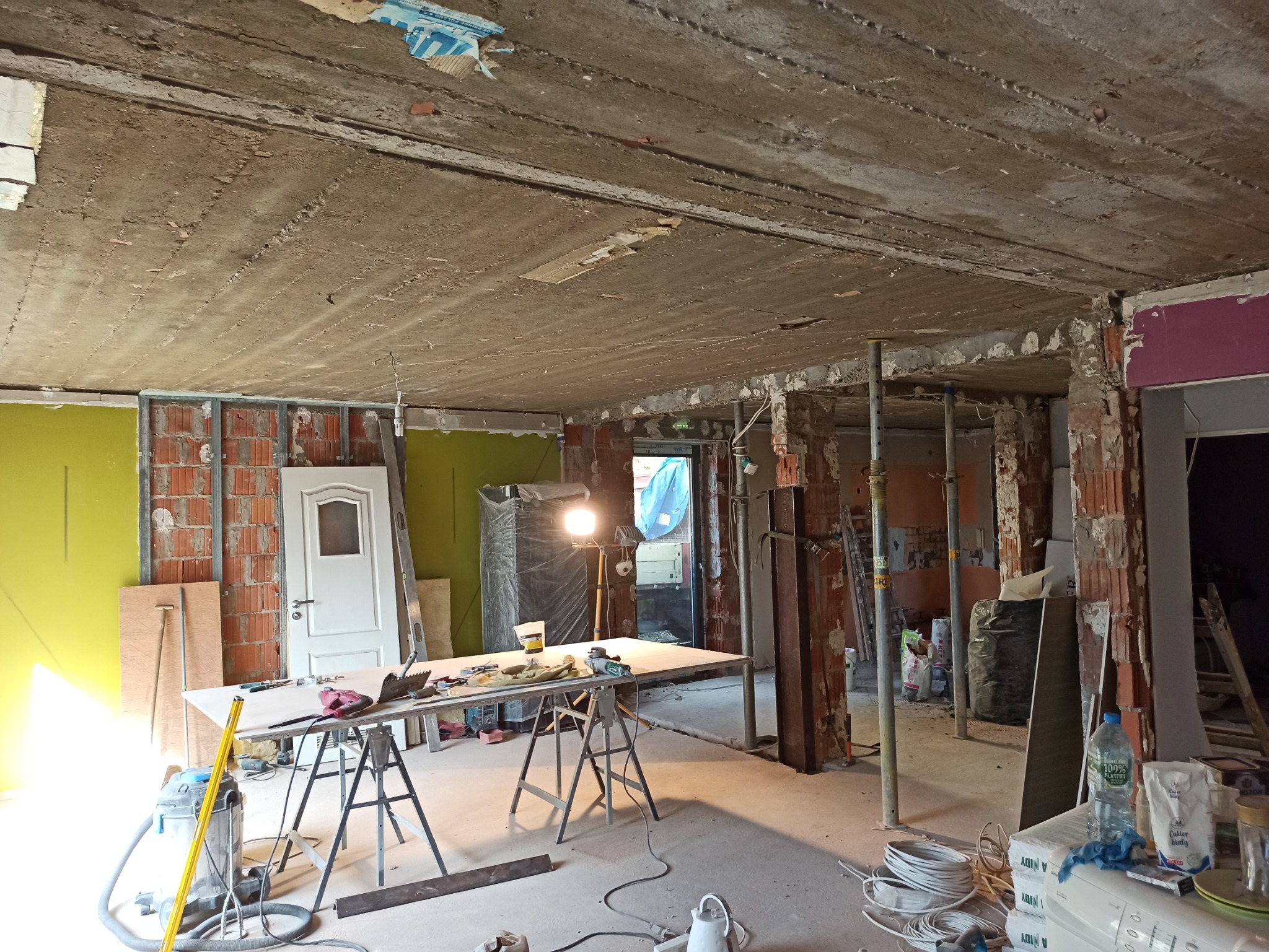 Stan surowy remontu w Częstochowie: przygotowanie do prac wykończeniowych, widoczne narzędzia, stół roboczy z akcesoriami, surowy betonowy strop i ściany z fragmentami instalacji.