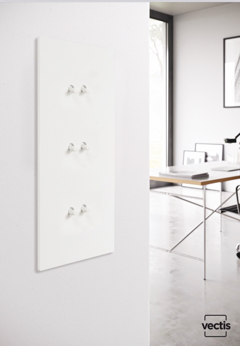 Biały panel z trzema rzędami haczyków zamontowany na ścianie w nowoczesnym wnętrzu biurowym z biurkiem i oknem w tle.