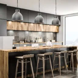 Nowoczesna kuchnia z drewnianym blatem, szarymi szafkami i trzema wiszącymi lampami w stylu industrialnym. W tle widoczne okno z panoramą miasta.