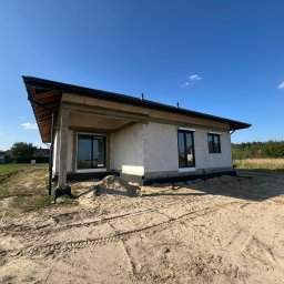 Okna LaVico Piotr Wontorczyk - Budowa domu jednorodzinnego w stanie surowym otwartym z zamontowanymi oknami z czarnymi ramami. Widok z zewnątrz na tle błękitnego nieba.