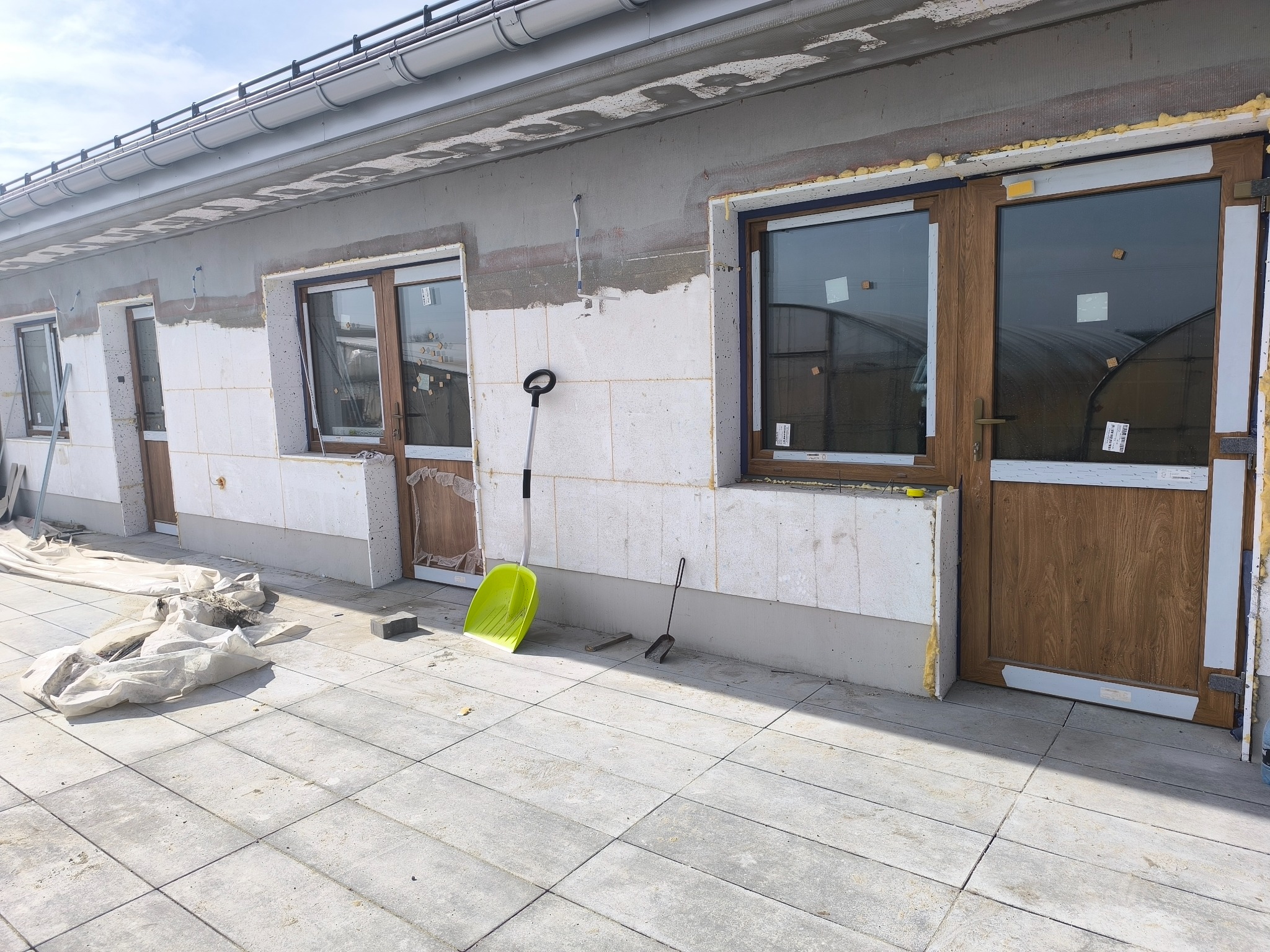 Montaż okien i drzwi zewnętrznych w domu jednorodzinnym, widoczne ocieplenie ścian, szpachelka i łopata na zewnątrz. Etap prac wykończeniowych.