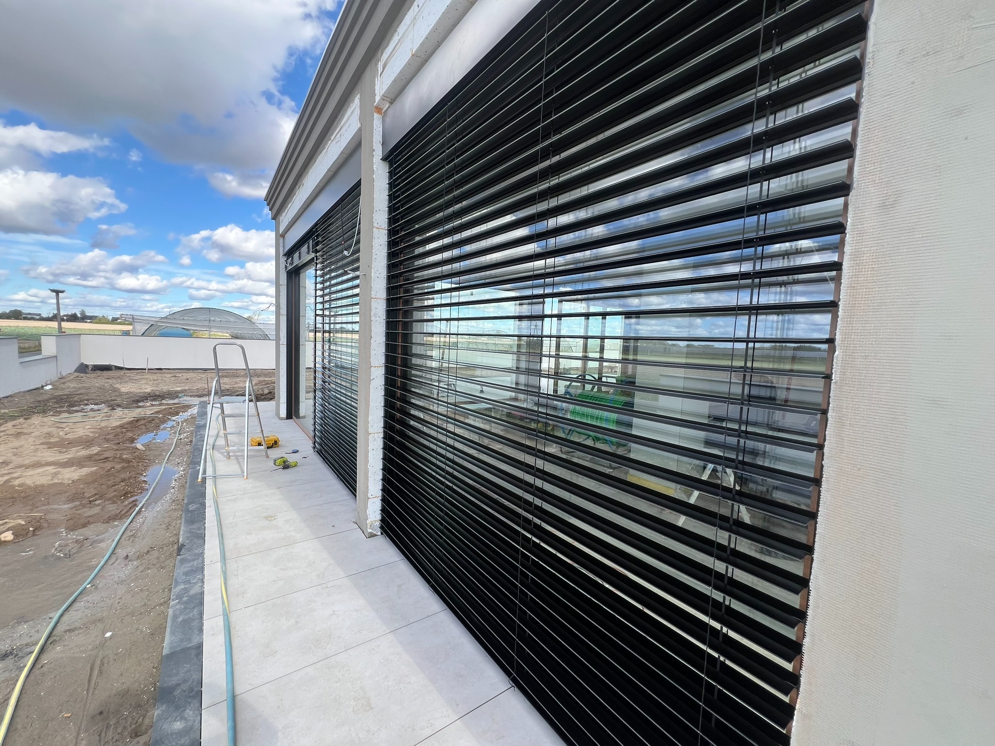 Czarne żaluzje zewnętrzne w Niechcicach, zamontowane na oknie budynku w trakcie budowy, z widocznymi narzędziami i drabiną.