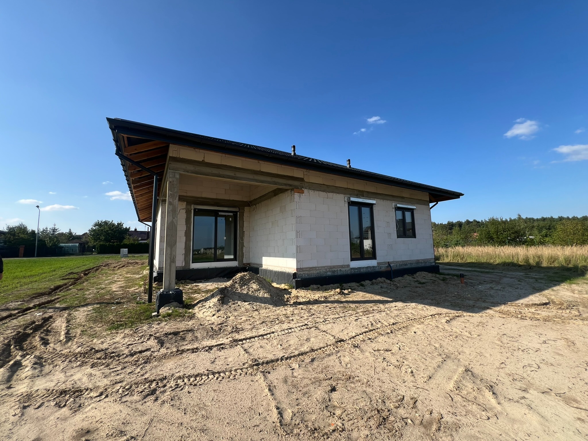 Budowa domu jednorodzinnego w stanie surowym otwartym z zamontowanymi oknami z czarnymi ramami. Widok z zewnątrz na tle błękitnego nieba.