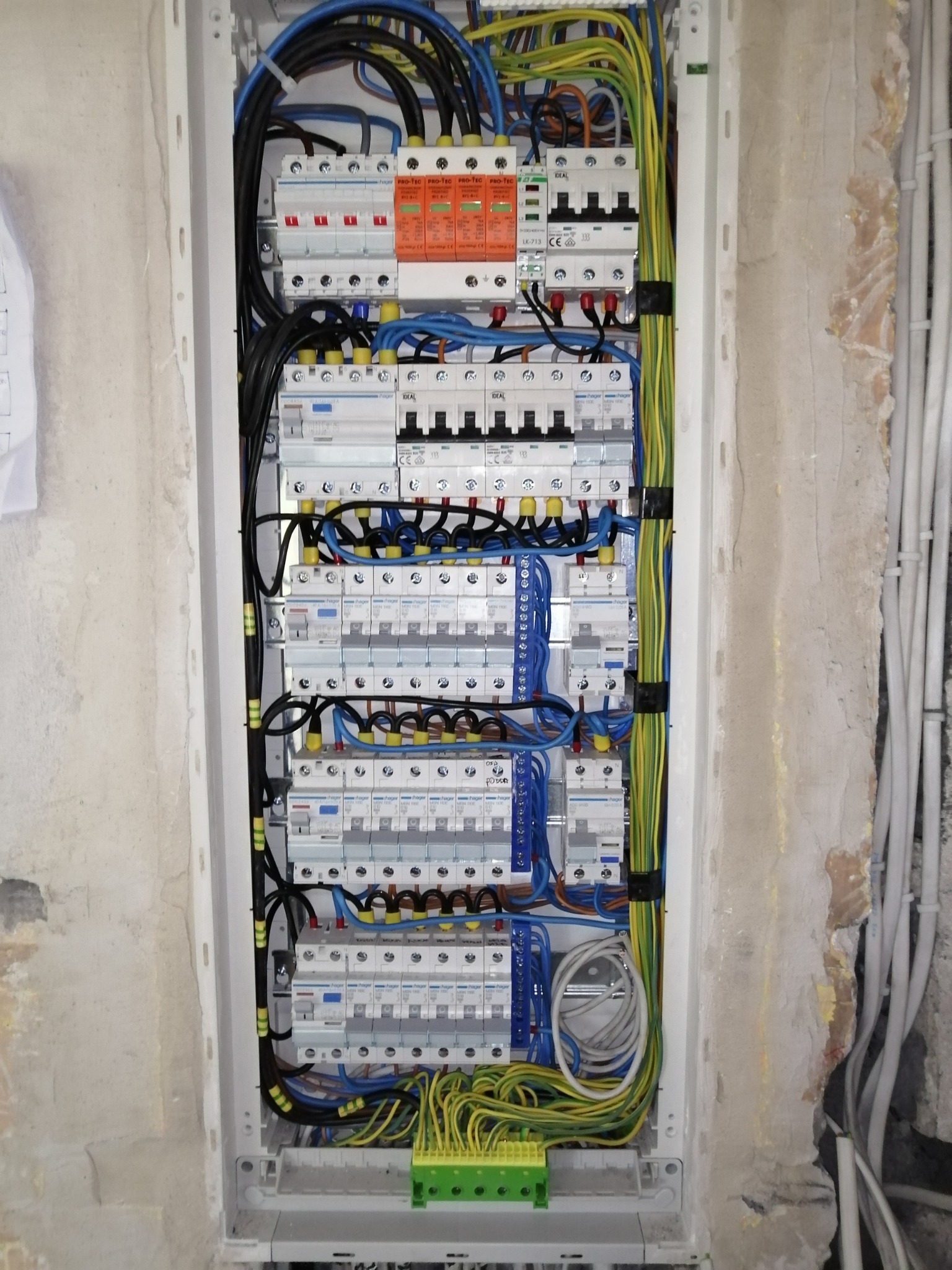 Rozdzielnica elektryczna z zainstalowanymi zabezpieczeniami różnicowoprądowymi i nadprądowymi, okablowana przewodami w kolorach żółto-zielonym, niebieskim i czarnym, zamontowana w ścianie...