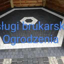 Wykończona podłoga altany z ciemnej kostki brukowej z jasnymi akcentami w kształcie wielokąta, widoczne drewniane słupy konstrukcyjne.