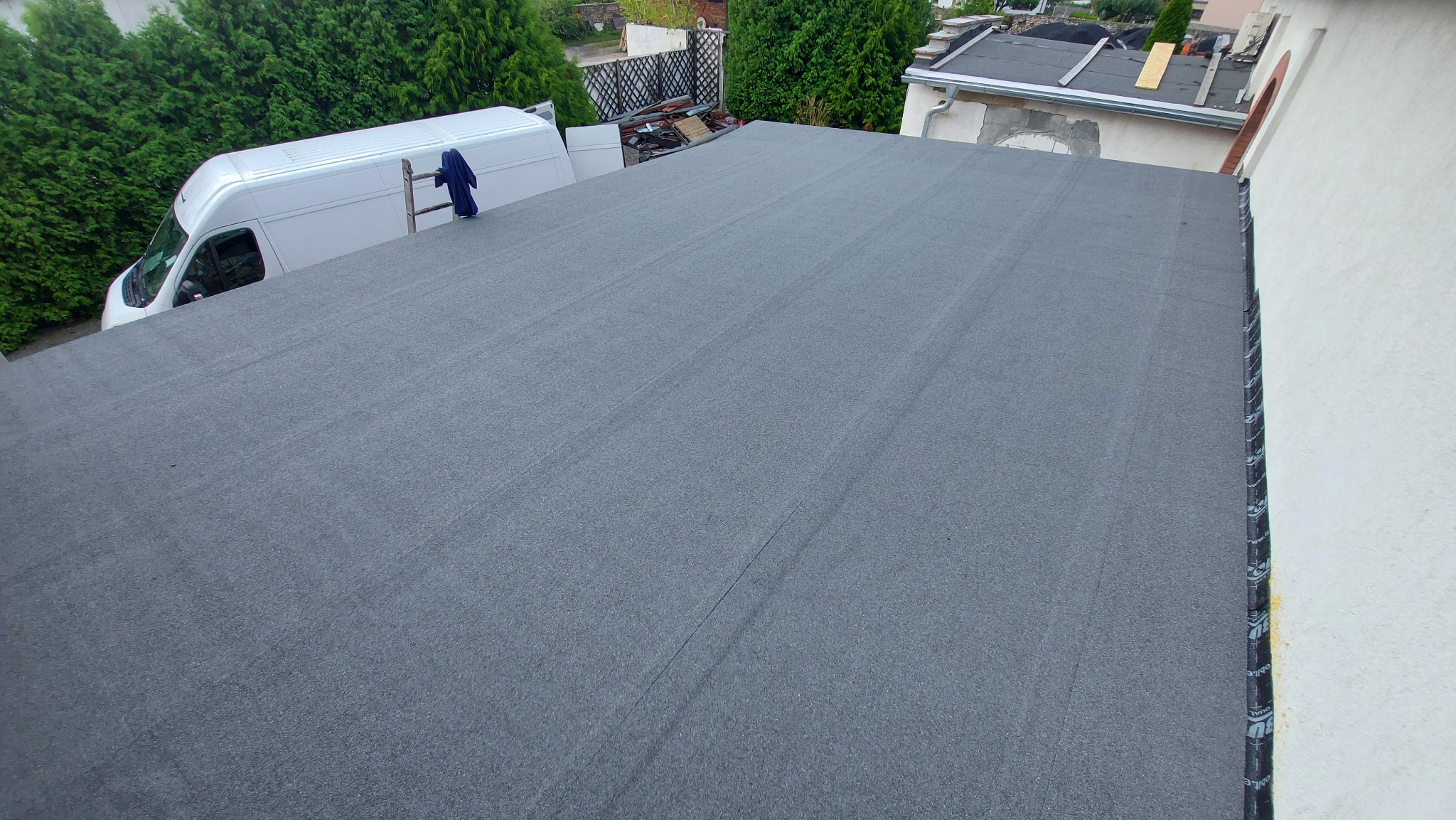 Nowo pokryty, płaski dach papą termozgrzewalną w Gliwicach, widok z góry, z białym samochodem dostawczym i drabiną w tle.