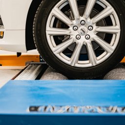 Okręgowa Stacja Kontroli Pojazdów Oblas - Biały samochód, prawdopodobnie Volvo, na stanowisku rolkowym w Oblas, podczas testu hamulców; widoczne koło i fragment nadwozia.