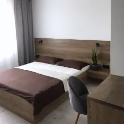 Nowoczesna sypialnia z drewnianym łóżkiem, szafką nocną z lampką i rośliną, szarą zasłoną i krzesłem na drewnianej podłodze.