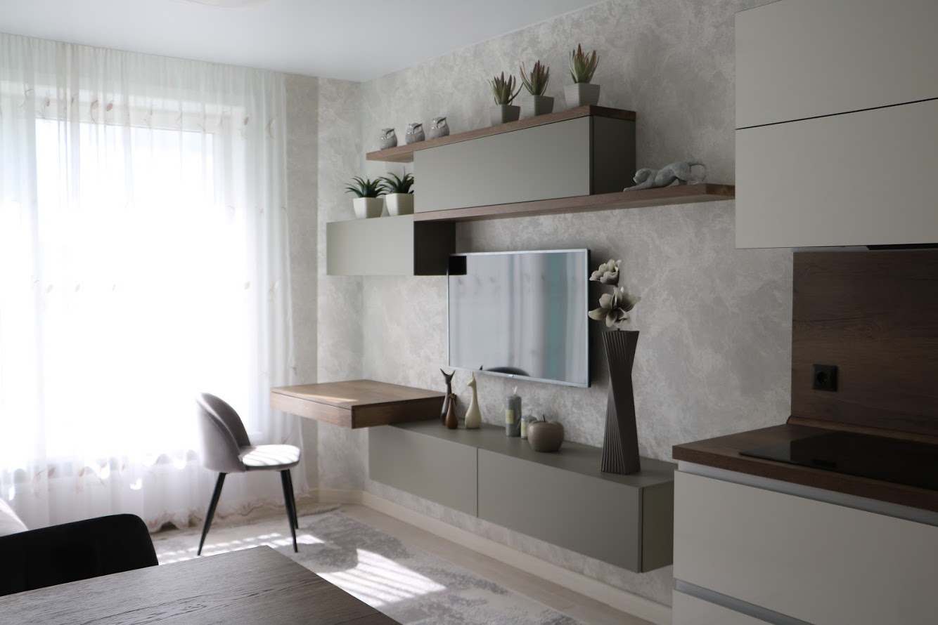 Nowoczesna aranżacja salonu we Wrocławiu z telewizorem wkomponowanym w system szafek wiszących i półek, uzupełniona o biurko i dekoracje.