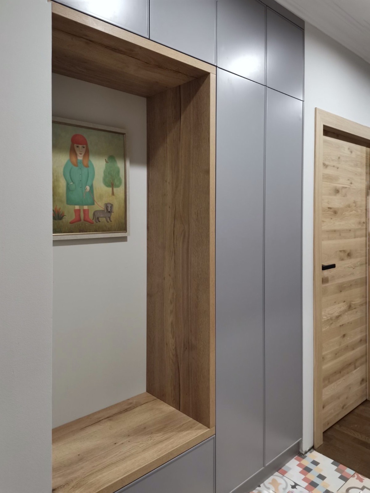 Szara szafa na wymiar z drewnianym regałem i obrazkiem dziewczynki z psem, drewniane drzwi w tle