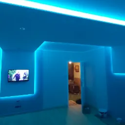 Pokój z nowoczesnym oświetleniem LED w kolorze niebieskim, tworzącym efektowną ramę wokół telewizora i wzdłuż sufitu, świeżo pomalowane ściany.