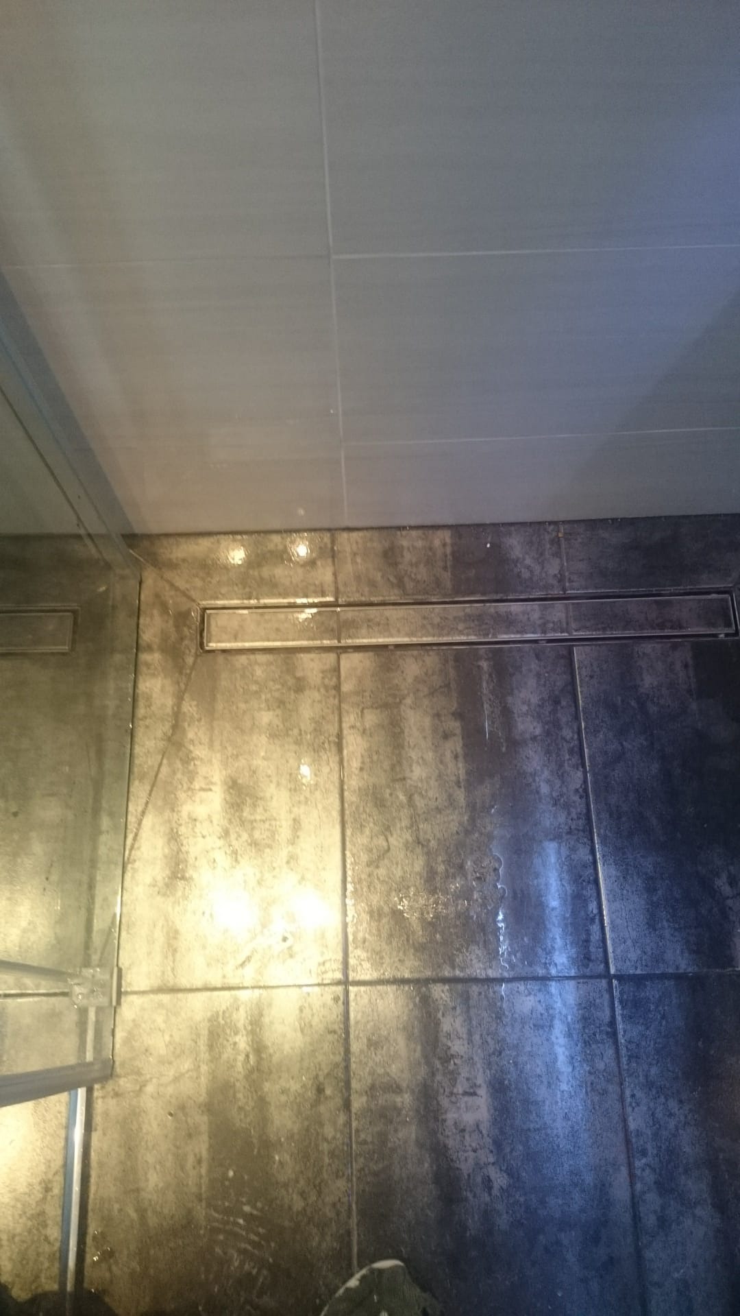 Nowoczesny odpływ liniowy w kabinie prysznicowej z ciemną, strukturalną płytką podłogową i jasną płytką ścienną.