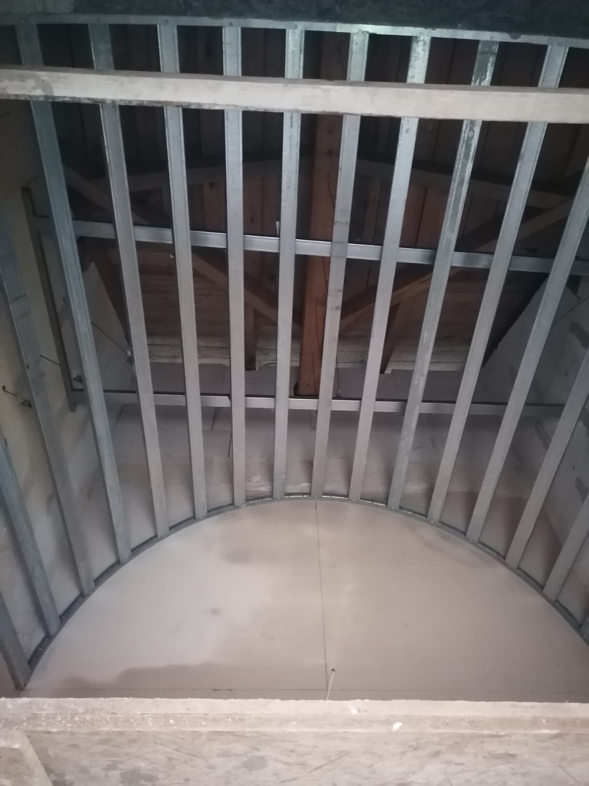 Konstrukcja sufitu podwieszanego z profili metalowych, widok od dołu, częściowo pokryta płytami gipsowo-kartonowymi tworzącymi łuk.