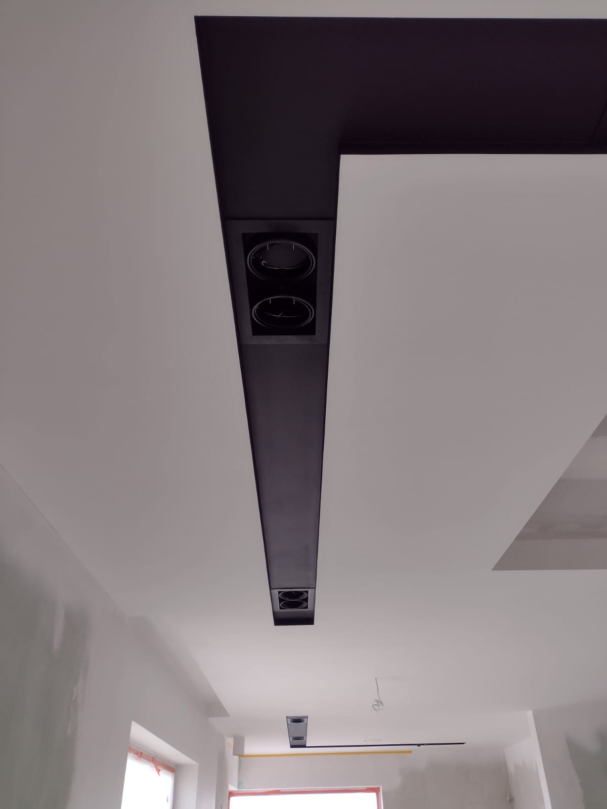 Sufit podwieszany z czarną listwą oświetleniową i wbudowanymi reflektorami, w trakcie prac wykończeniowych.