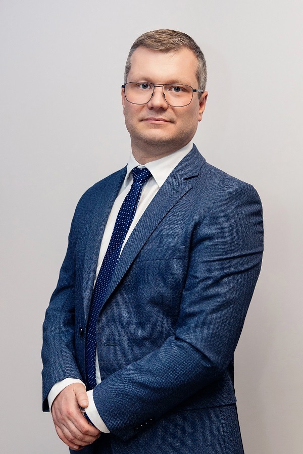 Portret mężczyzny w okularach i niebieskim garniturze z krawatem w Zielonej Górze, stojącego na jasnym tle.