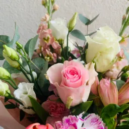 Delikatny bukiet z różowych i białych róż, goździków z fioletowymi żyłkami, tulipanów oraz zielonych pąków eustomy i eukaliptusa na rozmytym, jasnym tle.