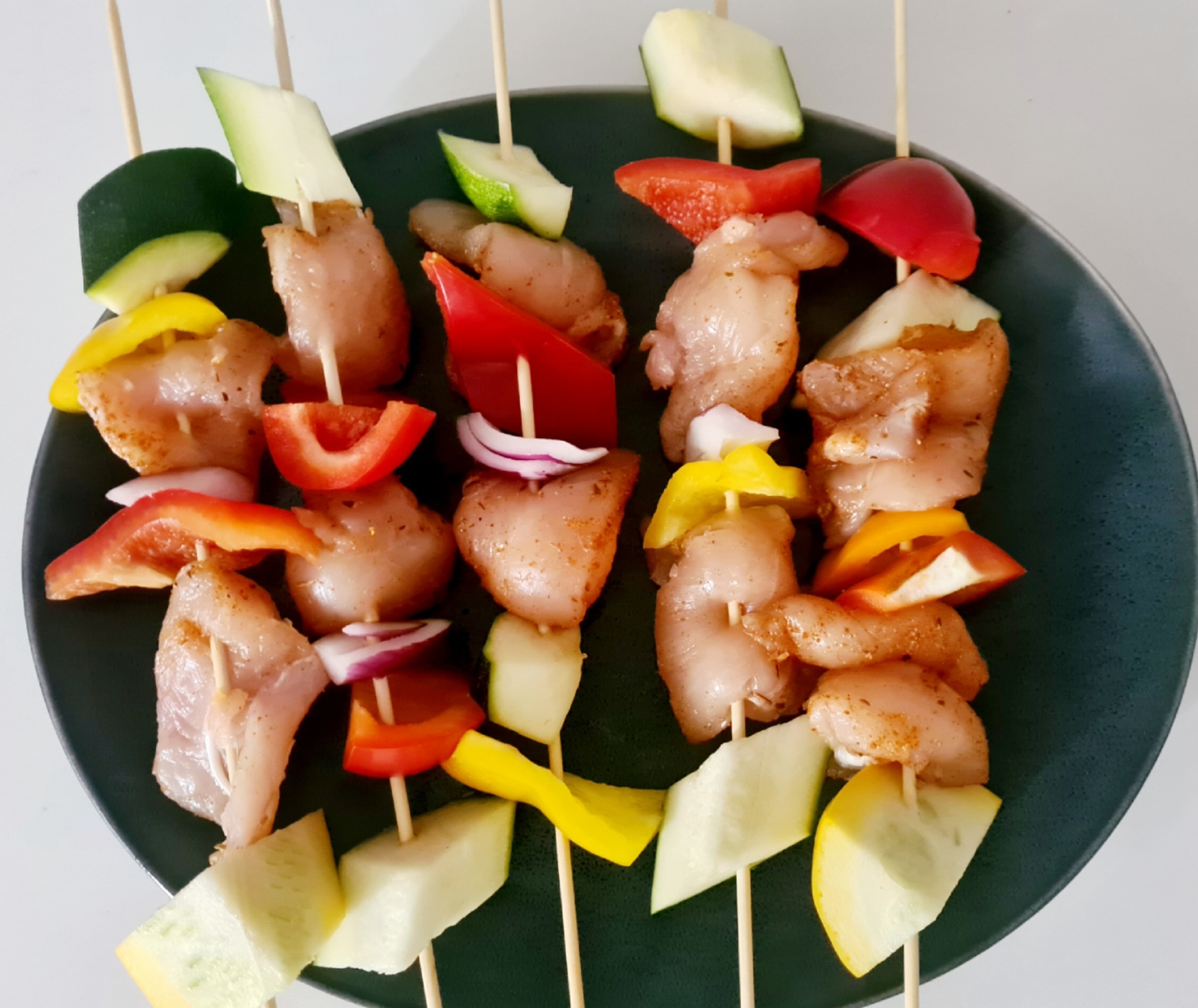 Szpadki z kurczakiem i warzywami (papryka, cebula, cukinia) na ciemnym talerzu, przygotowane do pieczenia lub grillowania.