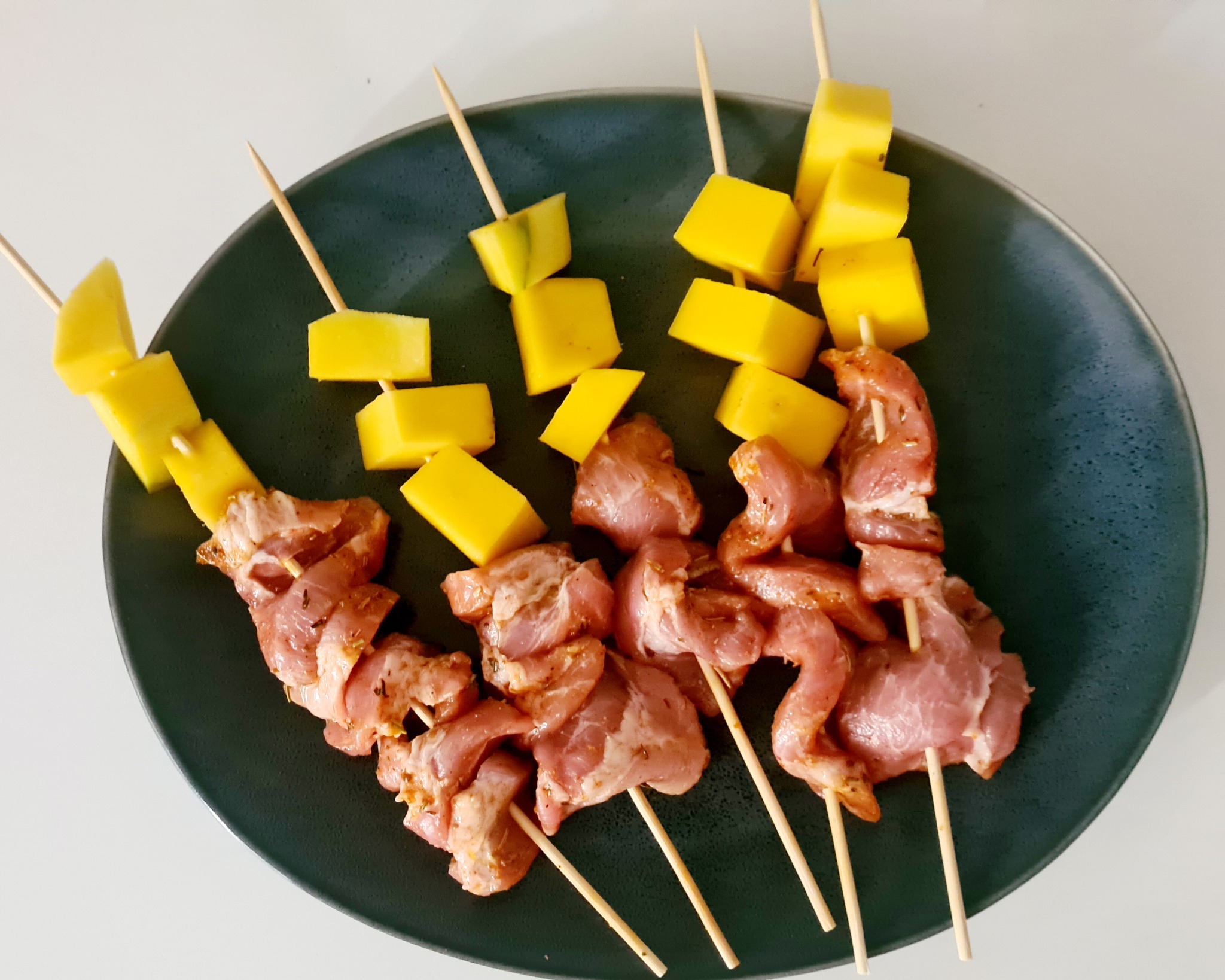 Szpadki z marynowaną surową wieprzowiną i kostkami mango na ciemnym talerzu