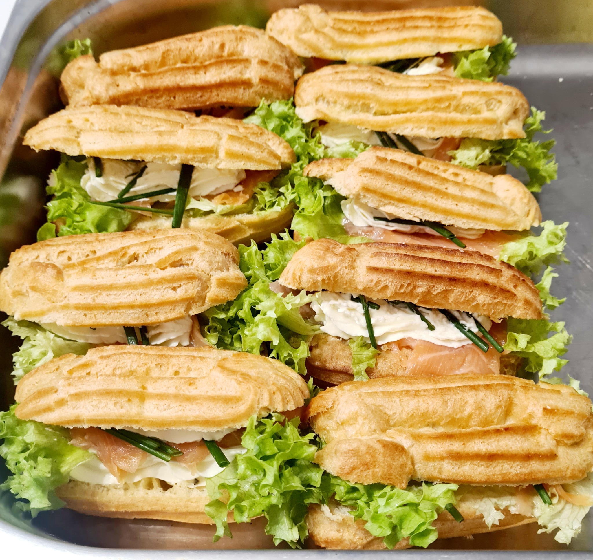 Eklery na słono z łososiem, kremem i sałatą, ułożone na metalowej tacy cateringowej.