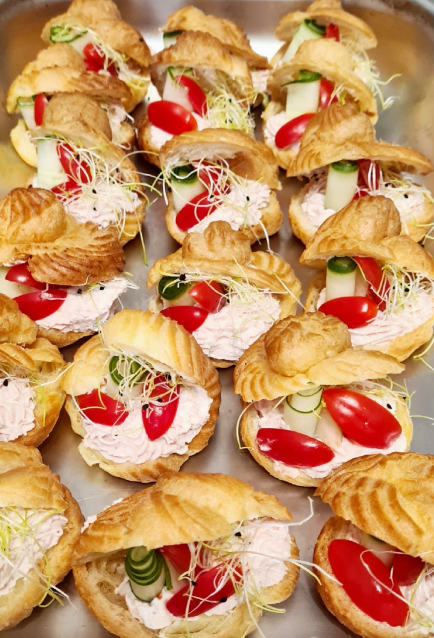 Taca z mini kanapeczkami na bazie ptysiów, wypełnionych kremowym farszem, dekorowanych połówkami pomidorków koktajlowych, plasterkami ogórka i świeżymi kiełkami.