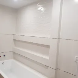 Nowoczesna łazienka z białą wanną, wnęką w ścianie wyłożonej płytkami z falistym wzorem i minimalistyczną armaturą.