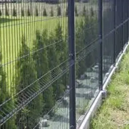 Nowoczesne ogrodzenie panelowe w kolorze grafitowym z podmurówką betonową, widok z zewnątrz na tle trawnika i szpaleru drzew iglastych.