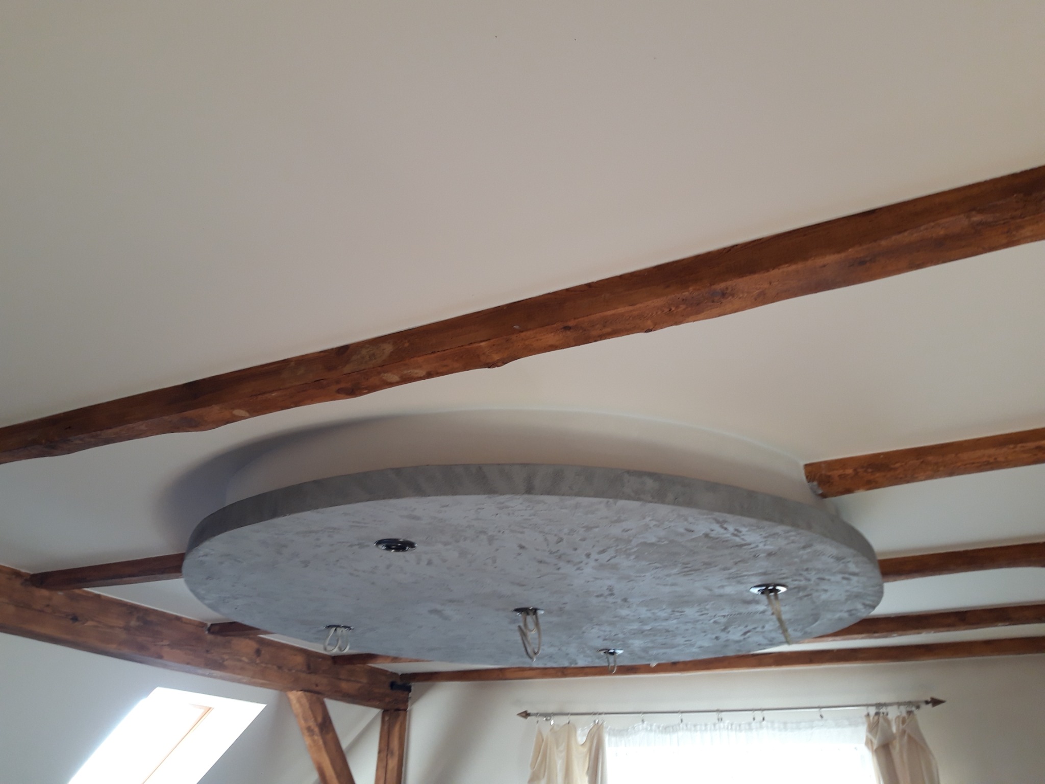 Wykończony sufit z okrągłą, betonową dekoracją w loftowym stylu, z widocznymi drewnianymi belkami stropowymi i otworami na oświetlenie.