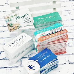 Copypoint - Stosy różnorodnych wizytówek z różnymi projektami graficznymi, ułożone na białym tle imitującym cegłę, prezentujące dane kontaktowe firm z branży florystycznej, rowerowej, fizjoterapii i kosmetycznej.